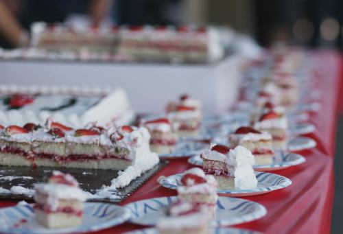 A table set with plates of layered cake topped with whipped cream and strawberries, alongside a larger cake.
