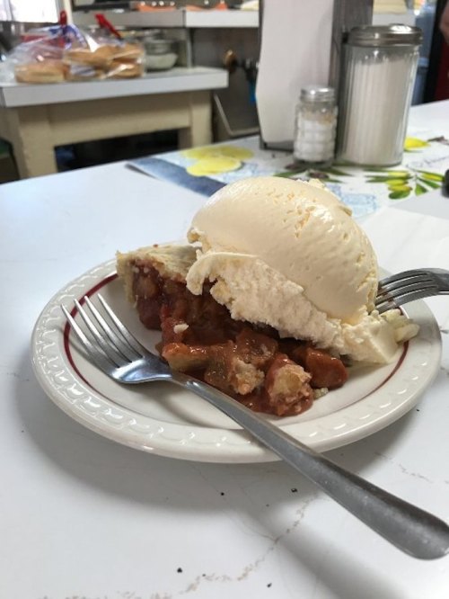 A slice of pie topped with a scoop of vanilla ice cream on a plate, with two forks beside it.