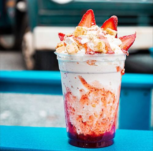 A delicious dessert cup filled with whipped cream, strawberries, and cake pieces, topped with a drizzle of sauce.