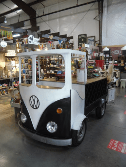 A vintage Volkswagen truck converted into a display stand inside a shop, surrounded by various items for sale.