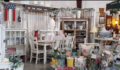 A cozy vintage shop display featuring white furniture, antiques, and decorative items in a rustic setting.
