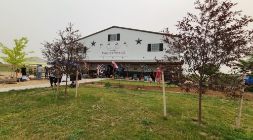 A vintage shop with a barn-style exterior, surrounded by trees and people enjoying the outdoor space.