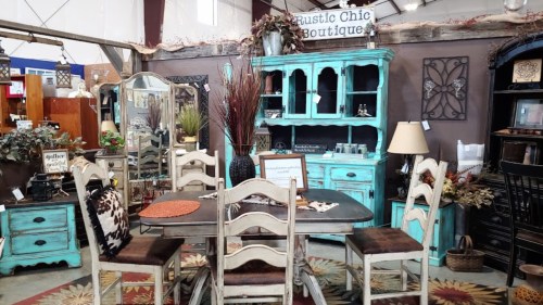 A rustic boutique display featuring a turquoise cabinet, wooden table, chairs, and decorative accents in a cozy setting.