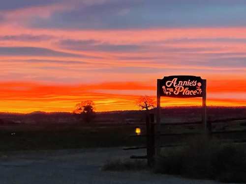 A sign for "Annie's Place" against a vibrant sunset with colorful clouds and silhouettes of trees.