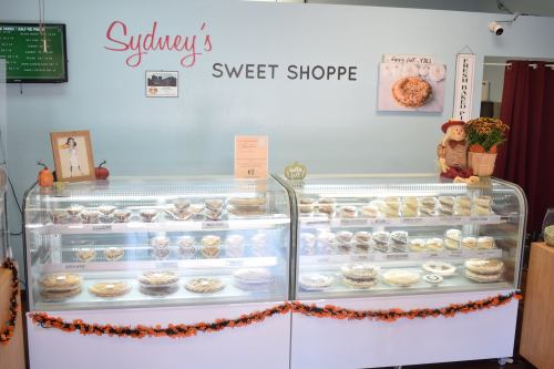 Display case filled with various baked goods at Sydney's Sweet Shoppe, decorated for fall with pumpkins and festive colors.