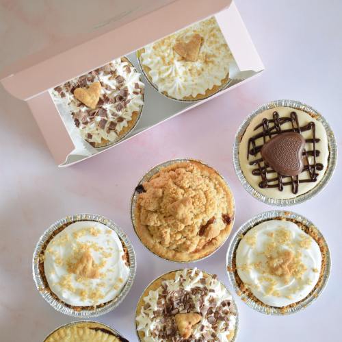 A variety of delicious cupcakes in a box, featuring different toppings and flavors, arranged on a light background.