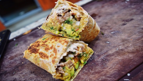 A delicious, stuffed burrito cut in half, revealing layers of meat, vegetables, and sauce on a wooden surface.
