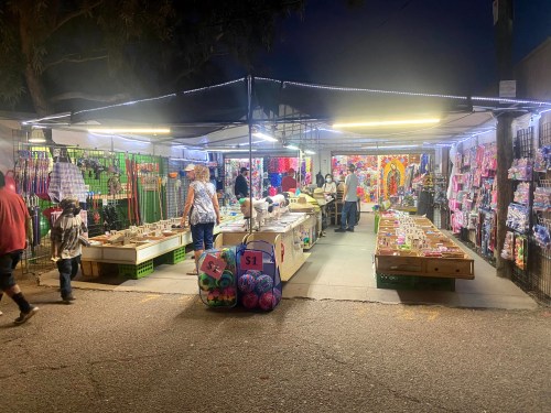 A vibrant night market with stalls selling various goods, colorful decorations, and shoppers browsing the merchandise.