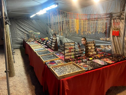 A jewelry market stall with various colorful bracelets, necklaces, and earrings displayed on tables under a tent.