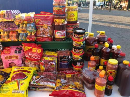 A colorful display of various snacks and condiments at a market stall, including chips, sauces, and sweets.