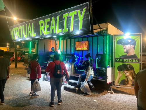 A vibrant virtual reality booth at night, featuring VR rides and people interacting with the setup.