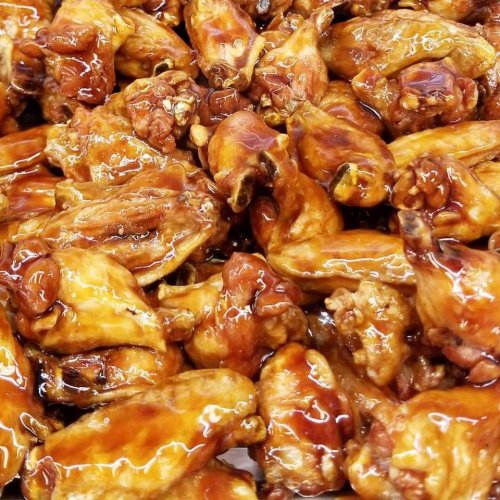 A close-up of golden-brown, glazed chicken wings piled together, showcasing a shiny, sticky coating.