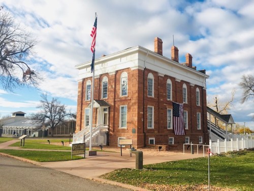 Historic building with red stone exterior, American flag, and grassy area under a partly cloudy sky.
