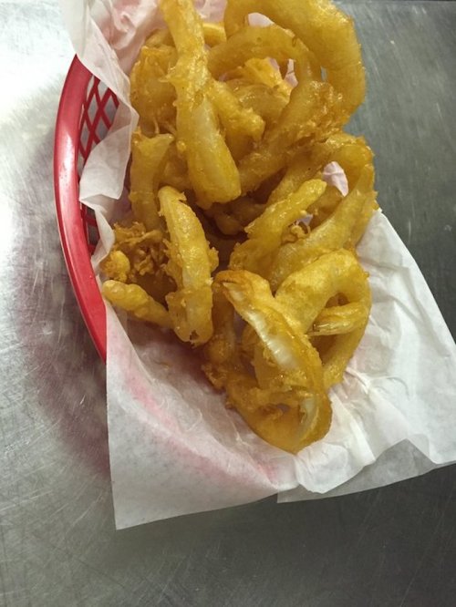 A red basket filled with golden, crispy fried onion rings on a paper liner.