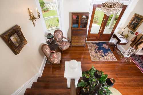 A cozy foyer with wooden floors, vintage furniture, a chandelier, and a view of the garden through large windows.