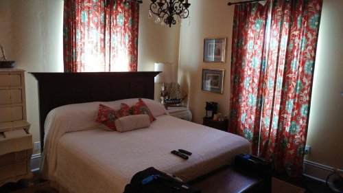 Cozy bedroom with a large bed, decorative pillows, red floral curtains, and a chandelier.