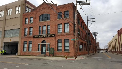 Historic Ford Piquette Plant building, a red brick structure with large windows, located on a city street.