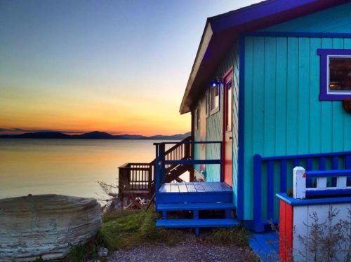 Colorful beach house at sunset, with a vibrant blue and turquoise exterior overlooking calm waters.