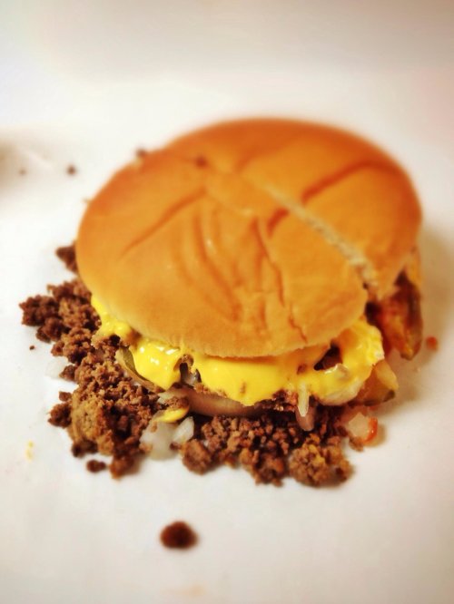 A cheeseburger with melted cheese and crumbled meat, partially split, on a white plate.