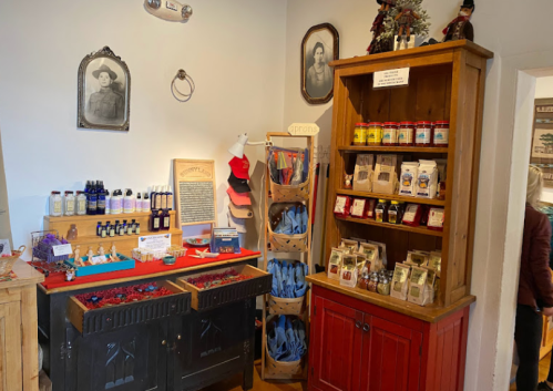 A cozy shop interior featuring shelves of products, jars, and framed portraits on the walls.