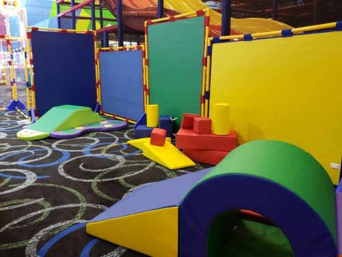 Colorful play area with soft, geometric shapes and climbing structures in a children's indoor playground.