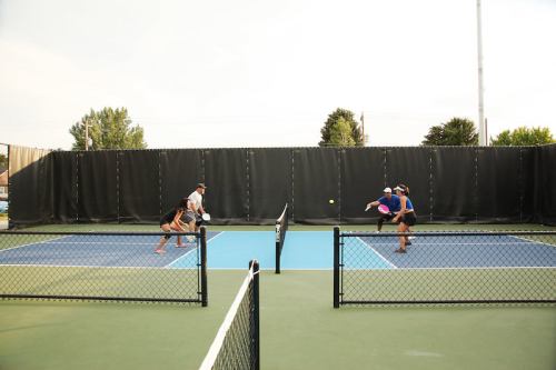 Two players engaged in a tennis match on a blue court, with a net and fencing in the background.