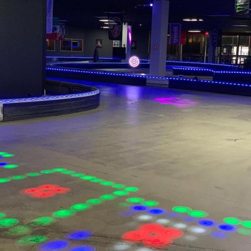 A brightly lit indoor go-kart track with colorful LED lights and a smooth, empty racing surface.