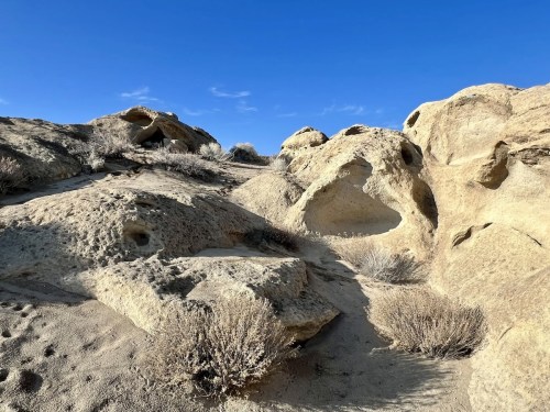 Rocky terrain with weathered formations and sparse vegetation under a clear blue sky.