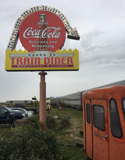 Sign for Santa Fe Train Diner with a vintage train car nearby, set against a cloudy sky.
