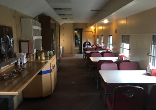 Interior of a vintage diner car with tables, chairs, and a counter, featuring warm lighting and a cozy atmosphere.