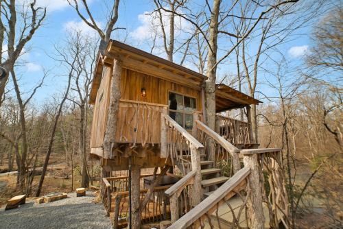 A rustic treehouse made of wood, elevated among bare trees, with a staircase leading up to a porch.