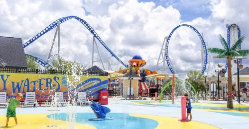 A vibrant water park scene with kids playing in fountains, roller coasters in the background, and colorful attractions.