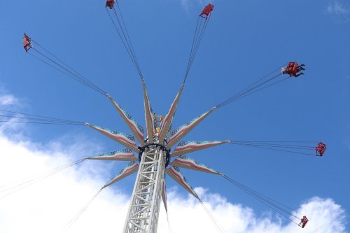 A colorful swing ride with seats suspended from a tall structure against a blue sky with clouds.