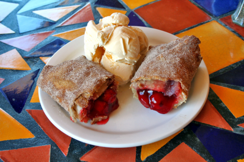 A plate with two cinnamon-sugar pastries filled with cherry filling, served alongside a scoop of vanilla ice cream.