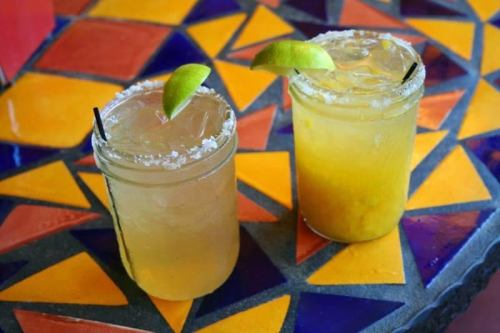 Two colorful cocktails with lime wedges on a vibrant, patterned table. One has a salted rim.
