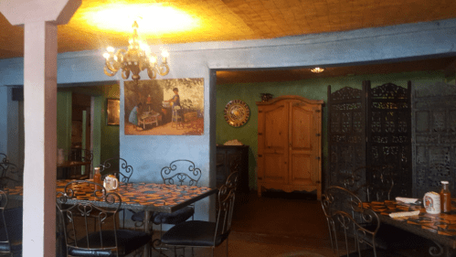 Cozy restaurant interior with colorful tables, decorative walls, and a wooden door, featuring a chandelier and artwork.