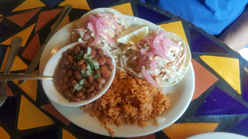 Two tacos topped with cabbage and pickled onions, served with rice and beans on a colorful table.