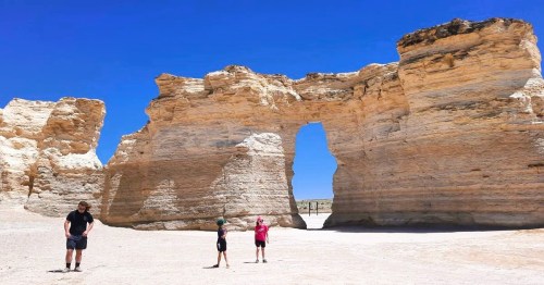 Visitors standing at Monument Rocks, a unique lookalike destination in Kansas countryside, featuring formations in a desert landscape.