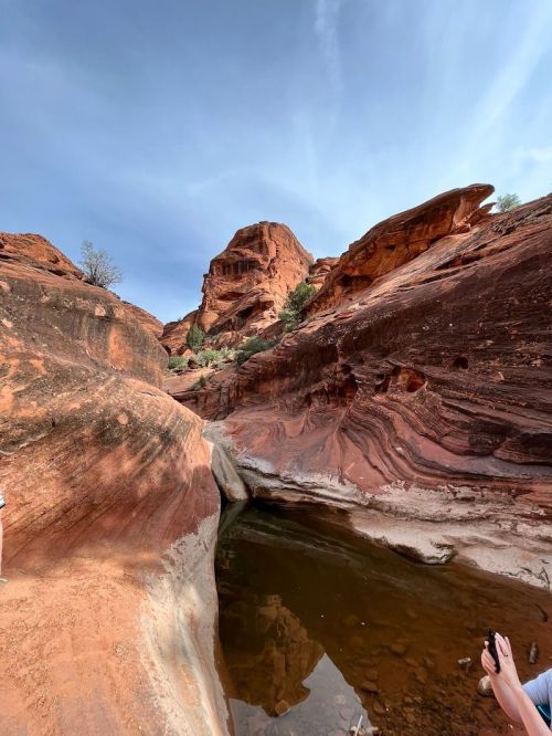A scenic view of red rock formations and a small pool of water under a blue sky.