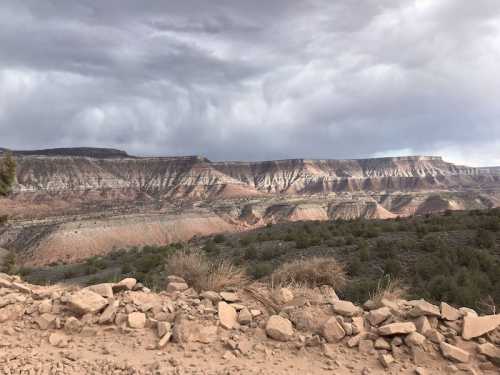 A rugged landscape featuring layered rock formations under a cloudy sky, with sparse vegetation in the foreground.