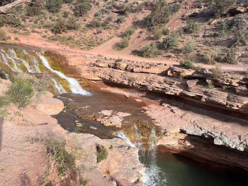 A scenic view of a rocky river with small waterfalls surrounded by dry vegetation and rugged terrain.