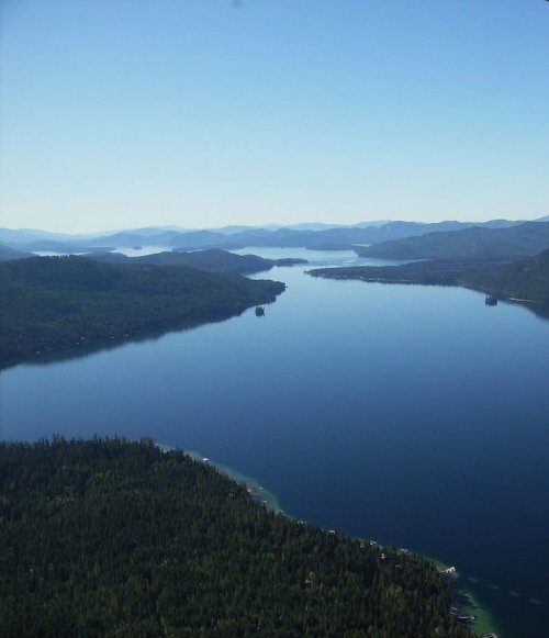 Aerial view of a serene lake surrounded by lush green mountains under a clear blue sky.