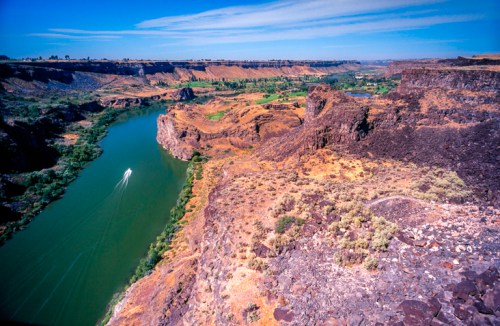 A scenic view of a river winding through rocky cliffs and green landscapes under a clear blue sky.