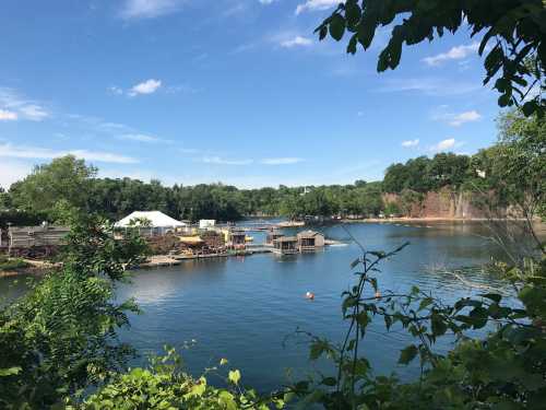 A serene lake surrounded by greenery, with boats and a dock under a clear blue sky.