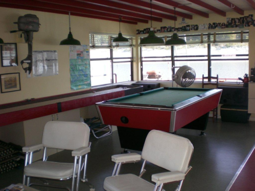 A game room featuring a pool table, two chairs, and large windows with a view of the outdoors.