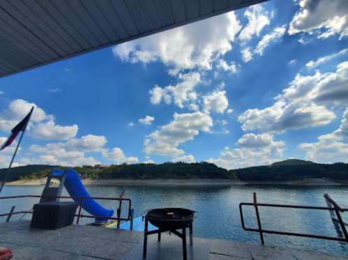 A scenic view of a lake with a blue slide, grill, and clouds in the sky, framed by a covered patio.