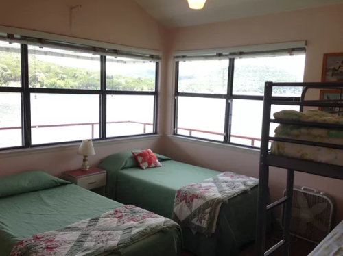 A cozy bedroom with two beds, a bunk bed, and large windows overlooking a scenic view of nature.