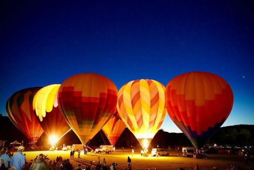 Colorful hot air balloons illuminated at night, surrounded by spectators in a festive atmosphere.