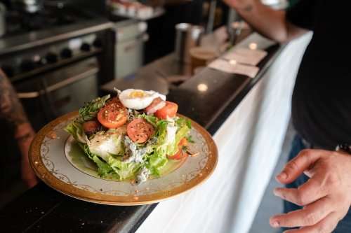 A colorful salad with lettuce, tomatoes, and a poached egg, served on a decorative plate at a restaurant counter.