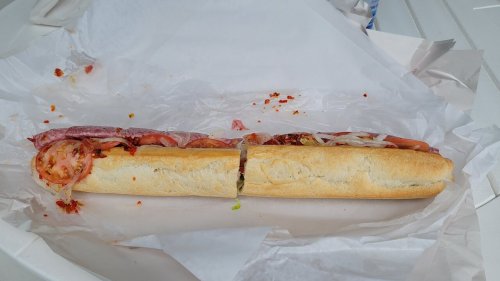 A sub sandwich filled with various meats, tomatoes, and onions, resting on white paper.